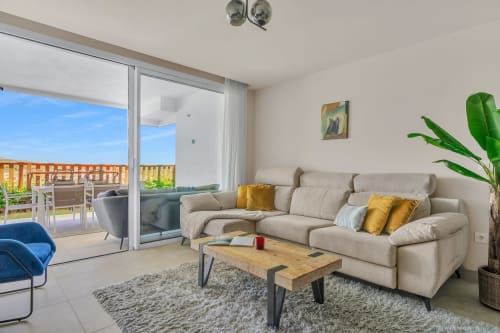 Nowoczesny salon apartamentu z beżową sofą, drewnianym stołem i widokami na góry w HomyMarbella w Elvirii, Hiszpania