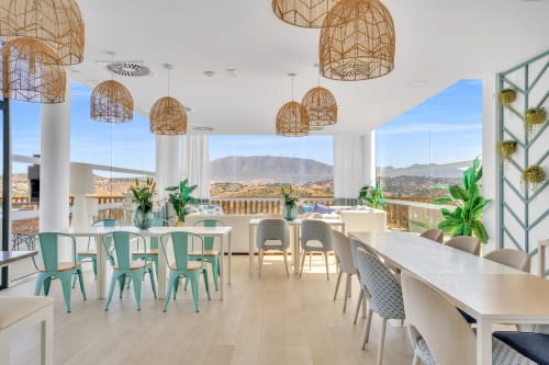 Nowoczesna jadalnia w apartamencie HomyMarbella Elviria z widokami na góry, wiszącymi lampami z plecionki i zielonymi akcentami