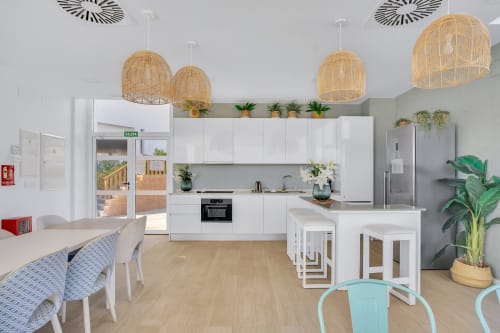 Nowoczesna kuchnia i jadalnia w apartamencie HomyMarbella w Elvirii z białymi szafkami, wiszącymi lampami z plecionką i widokiem na góry