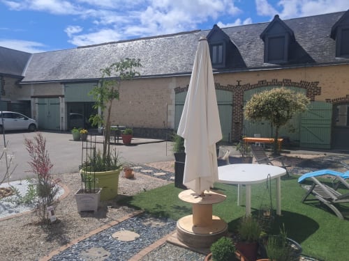 Jardin intérieur du gîte de la vallée à Courdemanche avec mobilier de terrasse, parasol et bâtiments en pierre