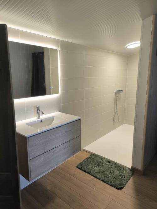Salle de bain moderne du Gite de la vallée à Courdemanche : miroir lumineux, lavabo blanc, murs carrelés, douche à l'italienne