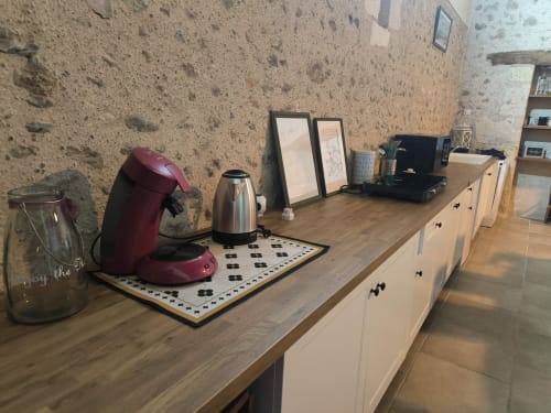 Plan de travail de cuisine rustique avec cafetière rouge, bouilloire et objets décoratifs contre un mur en pierre