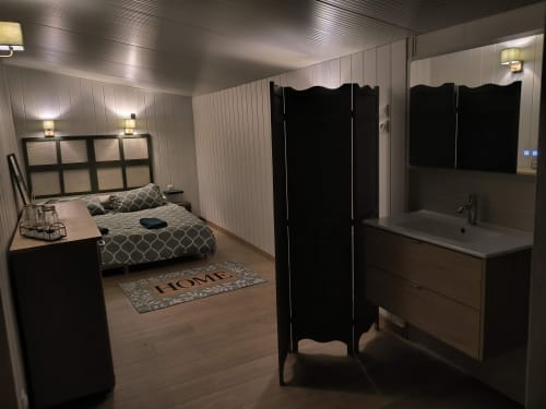 Chambre de cottage moderne avec salle de bains attenante, murs lambrissés blancs, lit avec literie à motifs et paravent noir