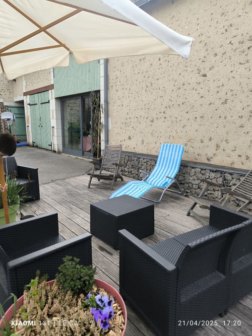 Terrasse du gîte de la vallée avec chaises longues à rayures bleues, mobilier en rotin noir, terrasse en bois et parasol crème