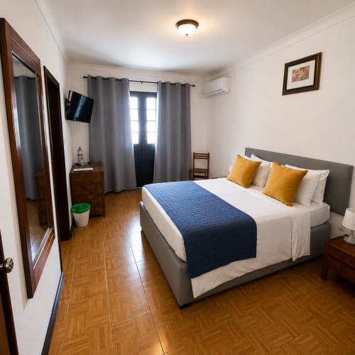 Quarto duplo da Serrana Gerês Inn com vista de montanha, cama cinza com almofadas amarelas, piso de madeira e comodidades modernas