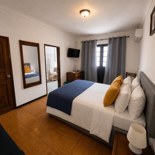 Quarto de casal amplo na Serrana Gerês Inn com roupa de cama branca, trilho azul, almofadas amarelas, espelhos de madeira e vistas para a montanha