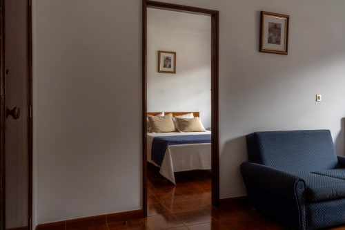 Quarto Duplo Standard na Pousada Serrana Gerês com espelho, cama, pisos de madeira e poltrona azul
