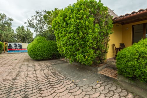 Rigogliose siepi verdi e giardino curato dell'hotel House Live Express a Quartu Sant'Elena, con edificio giallo e pavimentazione