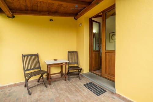 Terrazza con vista sul giardino, muri gialli, sedie in legno, tavolino e porta d'ingresso in legno presso House Live Express, Quartu