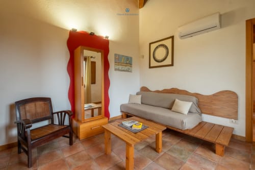 Zona living della Suite Locandiere presso House Live Express con divano in legno, poltrona, specchio e pavimentazione in cotto a Quartu