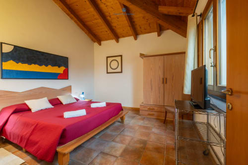 Camera Suite Locandiere presso House Live Express con letto rosso, travi in legno, TV e vista sul giardino a Quartu Sant'elena