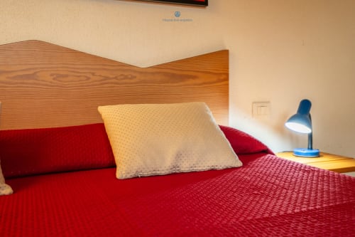 Camera accogliente in House Live Express con biancheria rossa, testata in legno, cuscino color crema e lampada da scrivania blu a Quartu Sant'Elena