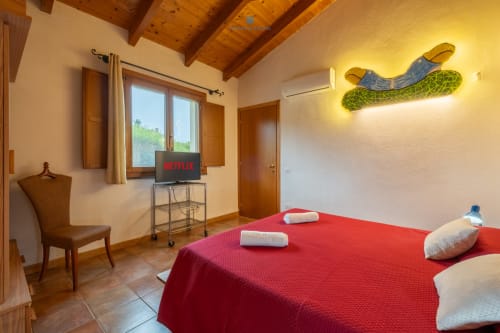 Camera Locandiere Suite presso House Live Express con letto rosso, TV, travi in legno e servizi moderni a Quartu Sant'elena