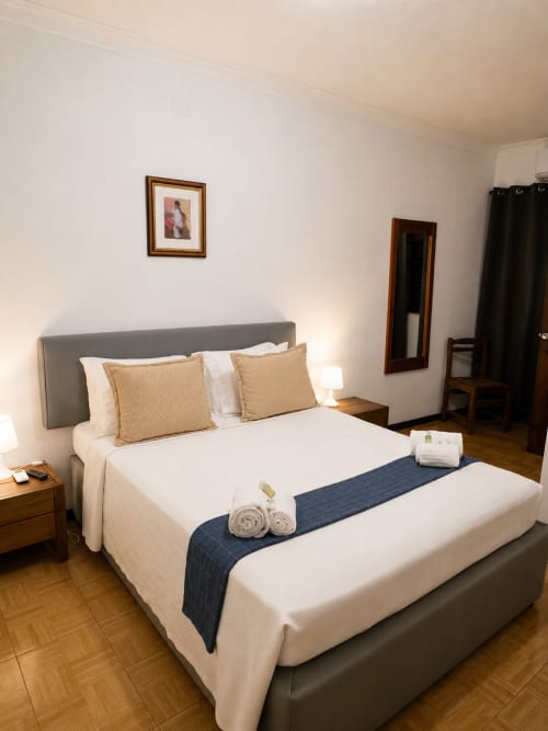 Quarto Duplo Standard da Pousada Serrana Gerês com cama estofada cinzenta, roupa de cama creme e criado de madeira