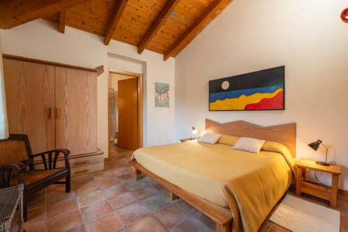 Camera della Suite Locandiere con travi in legno, pavimenti in cotto, biancheria gialla e opere d'arte colorate presso House Live Express