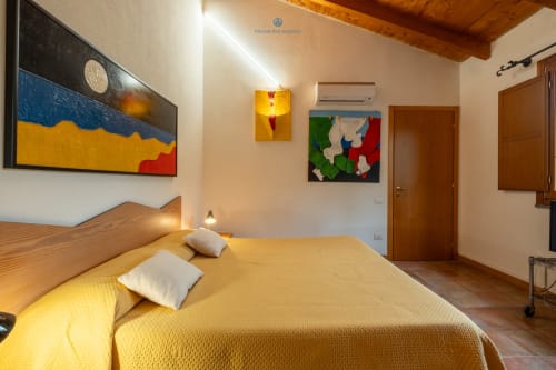 Camera Locandiere Suite presso House Live Express con biancheria gialla, mobili in legno, opere d'arte colorate e dotazioni moderne
