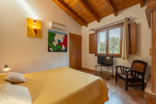 Camera luminosa nella Suite Locandiere di House Live Express, Quartu Sant'Elena, con coperta gialla, travi in legno, TV e