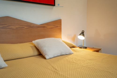 Camera da letto luminosa presso House Live Express con testata in legno, biancheria gialla, cuscini bianchi e lampada comodino a Quartu