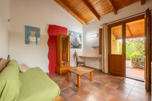 Suite Locandiere presso House Live Express con divano verde, arredamento in legno, pavimenti in cotto e porte con vista giardino a Quartu