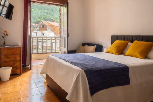 Quarto Duplo com Varanda na Pousada Serrana Gerês, vistas de montanha, cama com roupa de cama creme e almofadas amarelas, varanda com vista panorâmica
