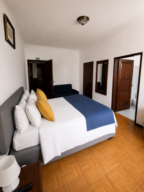 Espaçoso Quarto Standard Triplo na Pousada Serrana Gerês com cama queen, roupa de cama azul, piso de madeira e múltiplas portas