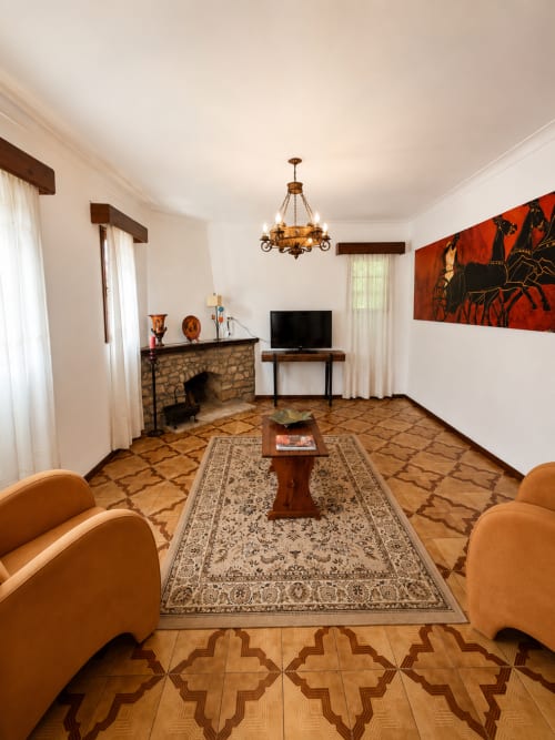 Sala de estar elegante na Pousada Serrana Gerês com lareira, poltronas de couro e vistas para as montanhas da varanda