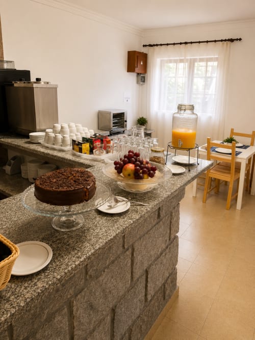 Cozinha da Pousada Serrana Gerês com bolo de chocolate, frutas frescas, suco e mesa preparada para hóspedes