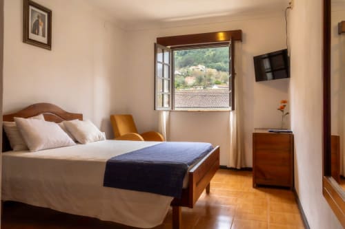 Quarto luminoso na Serrana Gerês Inn com cama de madeira, vista para as montanhas pela janela aberta, TV de tela plana e terracota