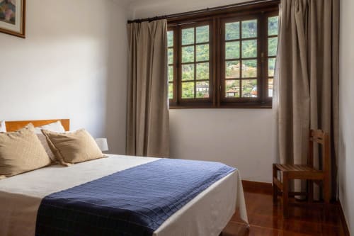 Quarto luminoso da Pousada Serrana Gerês com vista para a montanha, cama de madeira, cortinas bege e pisos em terracota em Gerês, Portugal