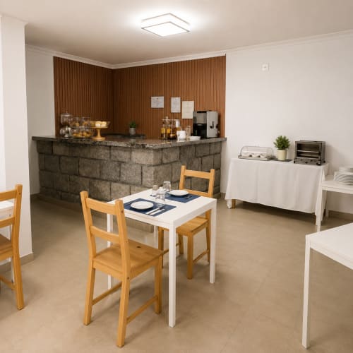 Sala de estar com área de refeições da Serrana Gerês Inn, cadeiras de madeira, vista para a montanha e comodidades de hospitalidade