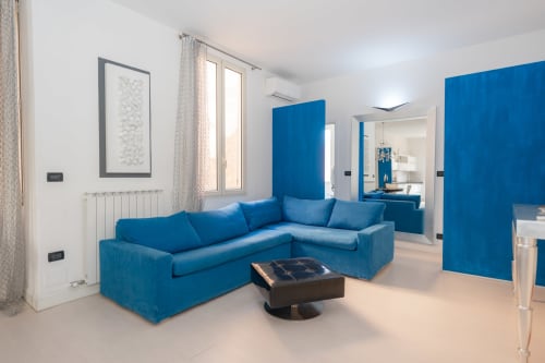 Divano angolare blu moderno nel luminoso salotto dell'appartamento Perla Marina a Finale Ligure con vista città e arredamento contemporaneo