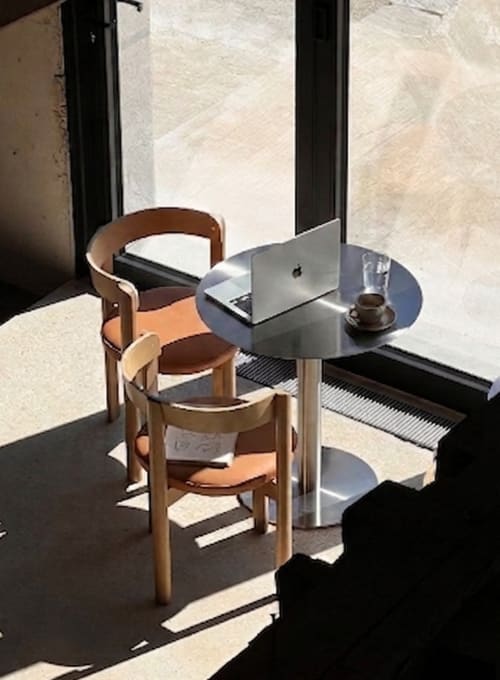 Espace de travail moderne au café du Moulin Moulin BnB à Dannes avec table ronde, chaises en bois et MacBook près de la fenêtre
