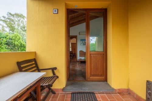 Portico giallo brillante con panchina in legno, ingresso principale e vista sul giardino della House Live Express a Quartu Sant'elena