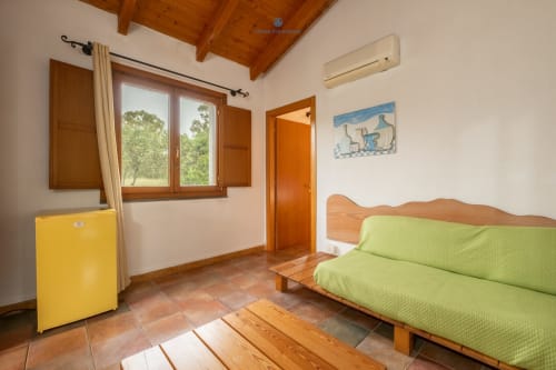 Camera con vista giardino presso House Live Express, con divano verde, arredi in legno e aria condizionata a Quartu Sant'Elena
