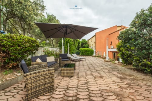 Terrazza House Live Express con sedute in vimini, ombrellone nero e vista giardino su edificio arancione a Quartu Sant'elena