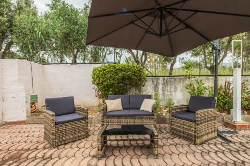 Area lounge esterna di House Live Express Quartu Sant'Elena con mobili in vimini e ombrellone marrone, vista giardino