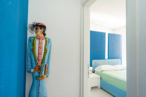 Statuetta decorativa colorata in abito blu davanti a parete azzurra brillante, appartamento Perla Marina a Finale Ligure