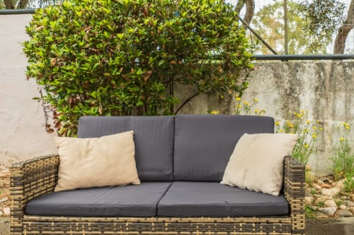 Divano in vimini con cuscini grigio e cuscini crema sulla terrazza del giardino di House Live Express, Quartu Sant'Elena