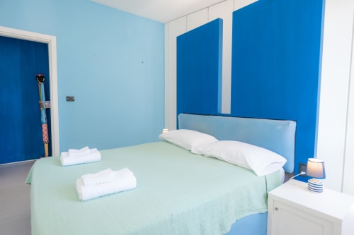 Camera da letto luminosa azzurra in appartamento a Finale Ligure con biancheria verde, cuscini bianchi e arredi moderni