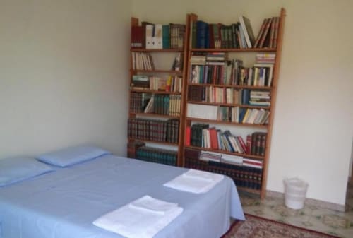 Camera da letto nella casetta di Bienbi Woods Three Houses con letto, biancheria bianca e libreria in legno a Boscotrecase