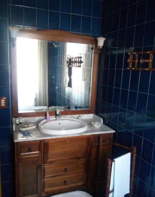 Bagno con lavabo rotondo, mobile in legno, specchio illuminato e piastrelle blu scuro presso il cottage Bienbi Woods
