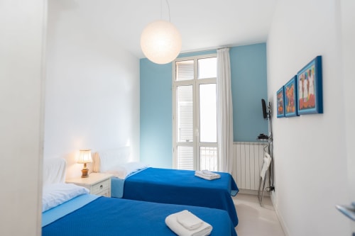 Due letti blu in luminoso appartamento di Varigotti con pareti turchesi, lampada a sospensione e balcone con vista sulla città presso Welcome Holiday