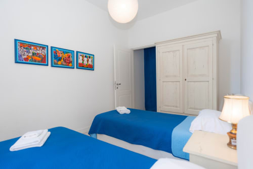 Camera doppia con letti blu, guardaroba bianco, opere d'arte e lampada nell'appartamento Perla Marina a Finale Ligure