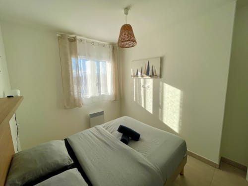 Bright bedroom at Marina di Bravone resort in Corsica with bed, woven pendant light, window with sea views