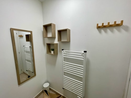 Modern bathroom at Résidence Marina di Bravone with wooden shelves, white towel rack, framed mirror, and wall hooks