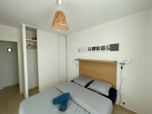 Modern bedroom at Résidence Marina di Bravone with wooden bed, woven pendant light, and built-in wardrobe