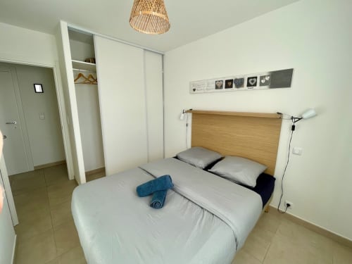 Modern bedroom at Résidence Marina di Bravone, Linguizzetta, with wooden headboard, white bedding, and wicker pendant light
