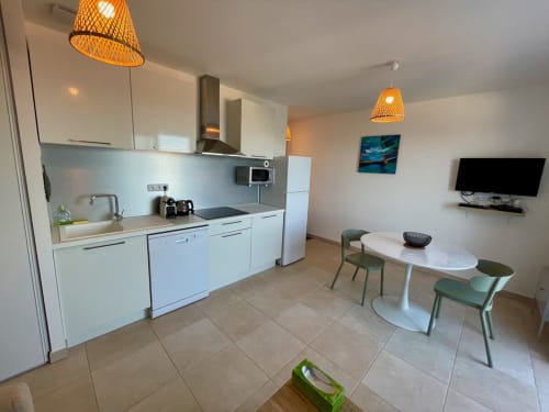 Modern kitchen-living area at Résidence Marina di Bravone, Linguizzetta with white cabinetry, dining table, and TV.