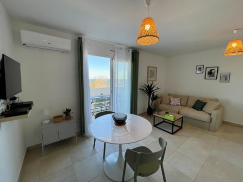 Modern apartment at Marina di Bravone with sea view terrace, round dining table, beige sofa, and woven pendant lights