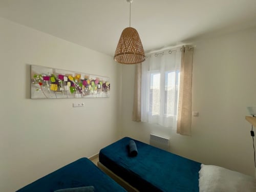 Marina di Bravone apartment bedroom with twin beds, woven pendant light, and colorful flower artwork